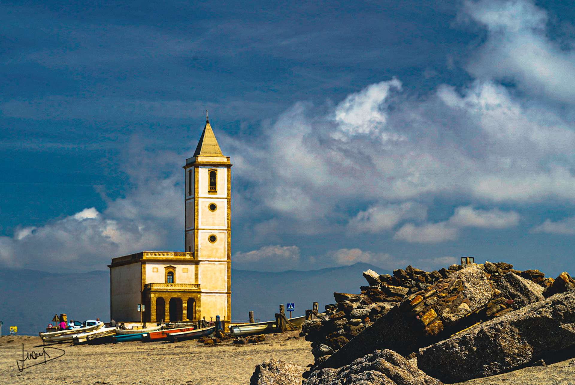 Vista de la iglesia de San Miguel en la Almadraba de Monteleva, Cabo de Gata. Un edificio religioso blanco y solitario con un campanario sencillo, situado en un paisaje llano y costero bajo un cielo despejado.